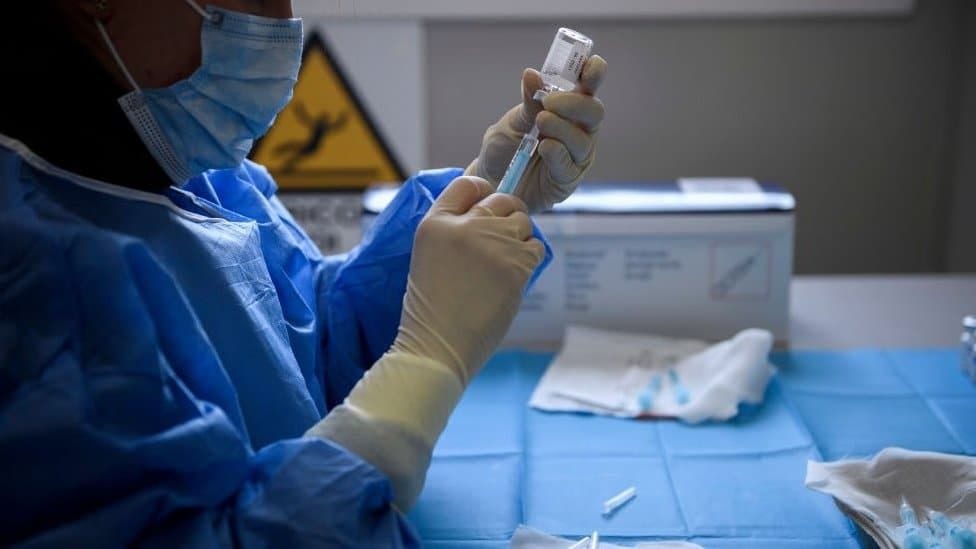 A person in PPE draws the vaccine from a vial into a syringe