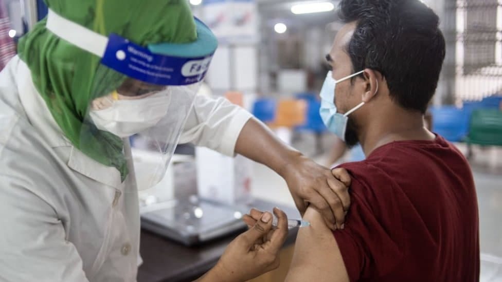 A man is vaccinated by a woman with a face shield in Bangladesh